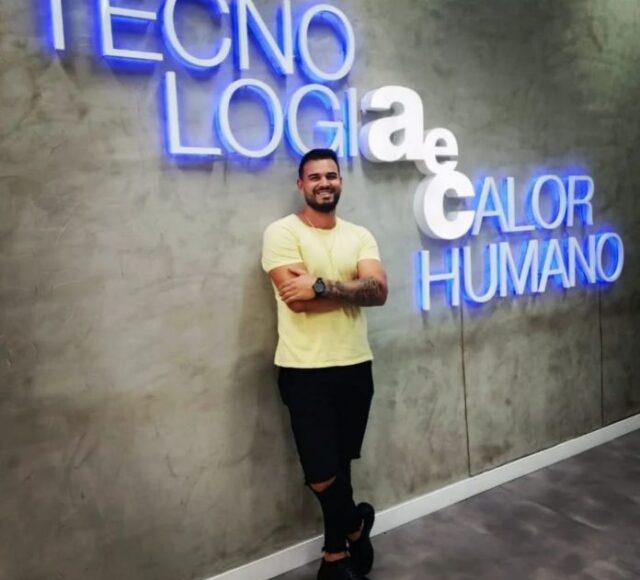 Colaborador Jamesson, da AeC, recostado na parede, com o letreiro Tecnologiaecalor humano na parede