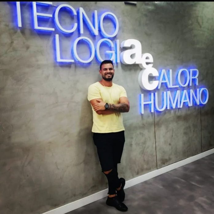 Colaborador Jamesson, da AeC, recostado na parede, com o letreiro Tecnologiaecalor humano na parede